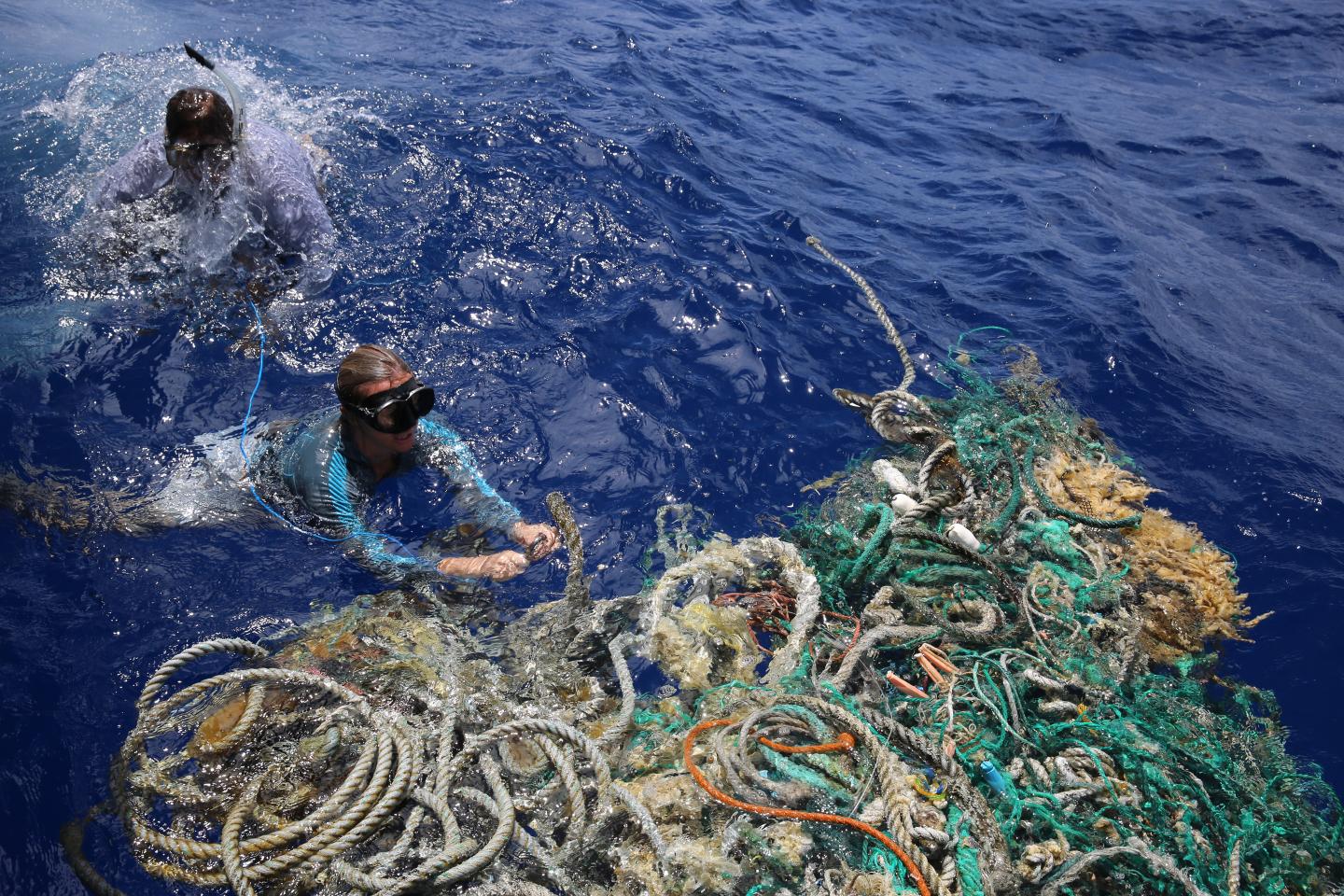 Divers in ocean next to a collection of debris