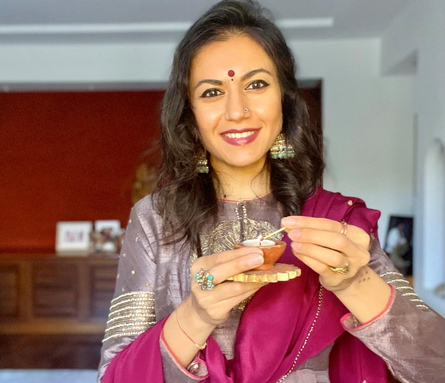 Portrait photo of chef and author Mira Manek. She is dressed in a sari and holding a match to a small tea light
