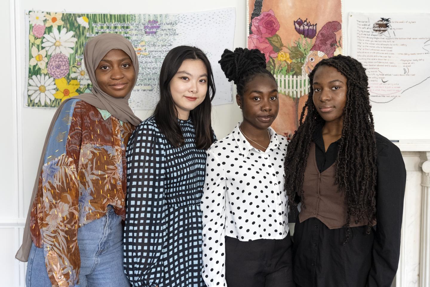 Four young people stand against a background of artwork