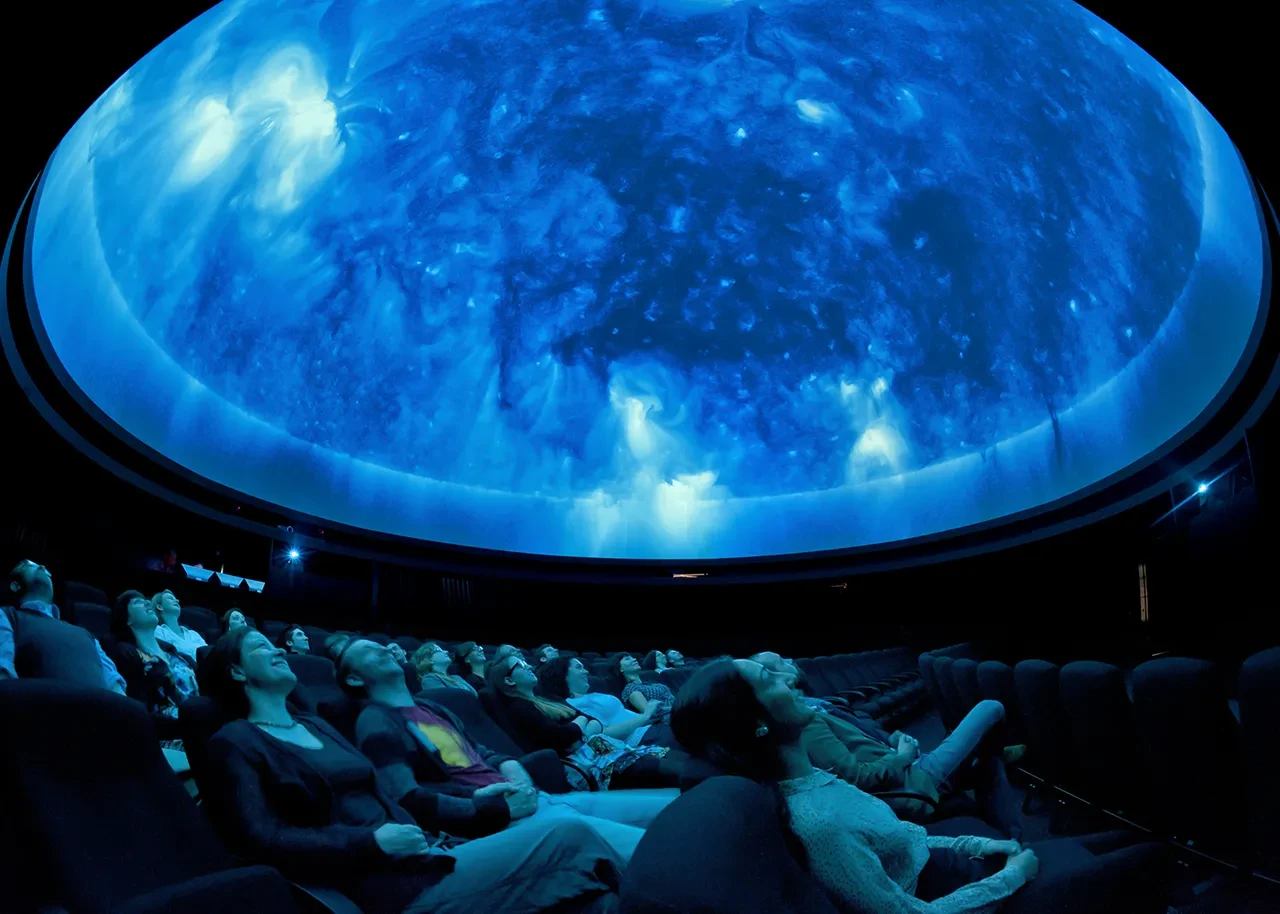 An audience staring up at a domed blue light projection of space.