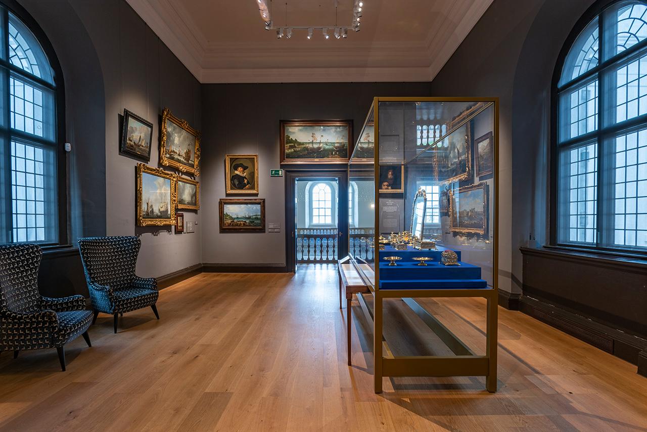 Interior of a room in the Queen's House with paintings on the wall and a cabinet in the centre of the room displaying Museum artefacts