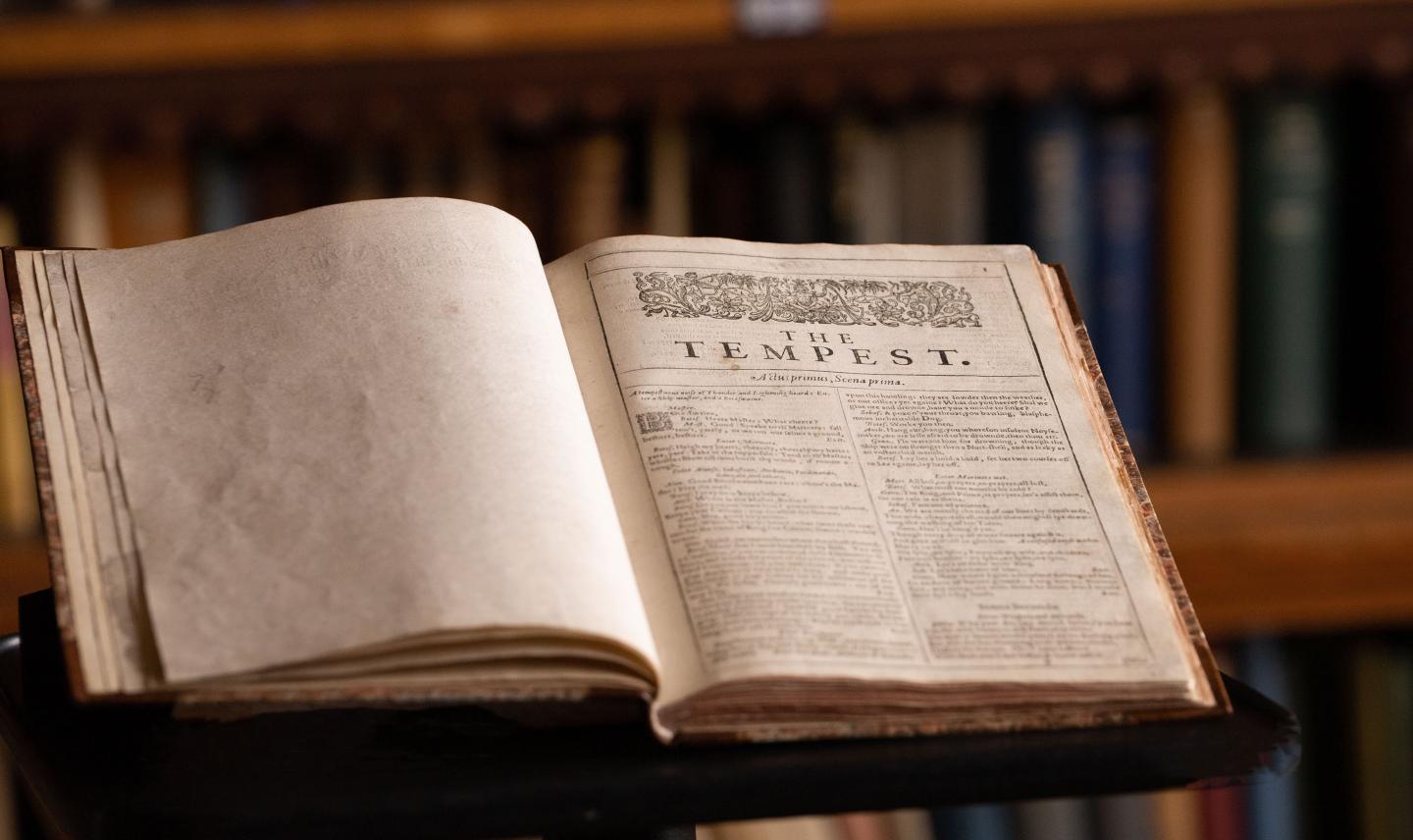 A photograph showing a page from Shakespeare's First Folio owned by Dulwich College. The edition is laid open at the first page of The Tempest, with shelves of books just visible in the background