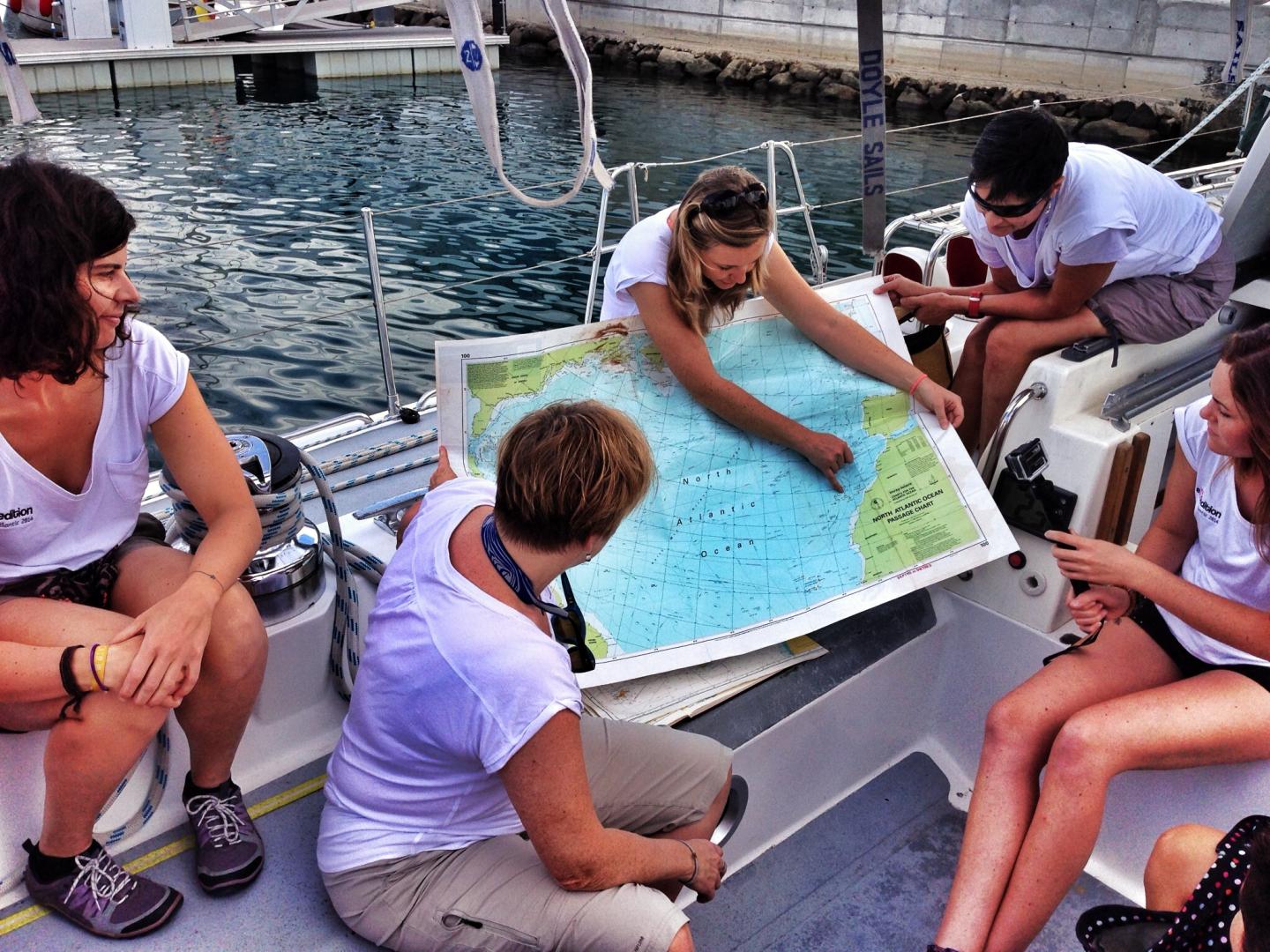 A group of women sit on the deck of a ship looking at a map