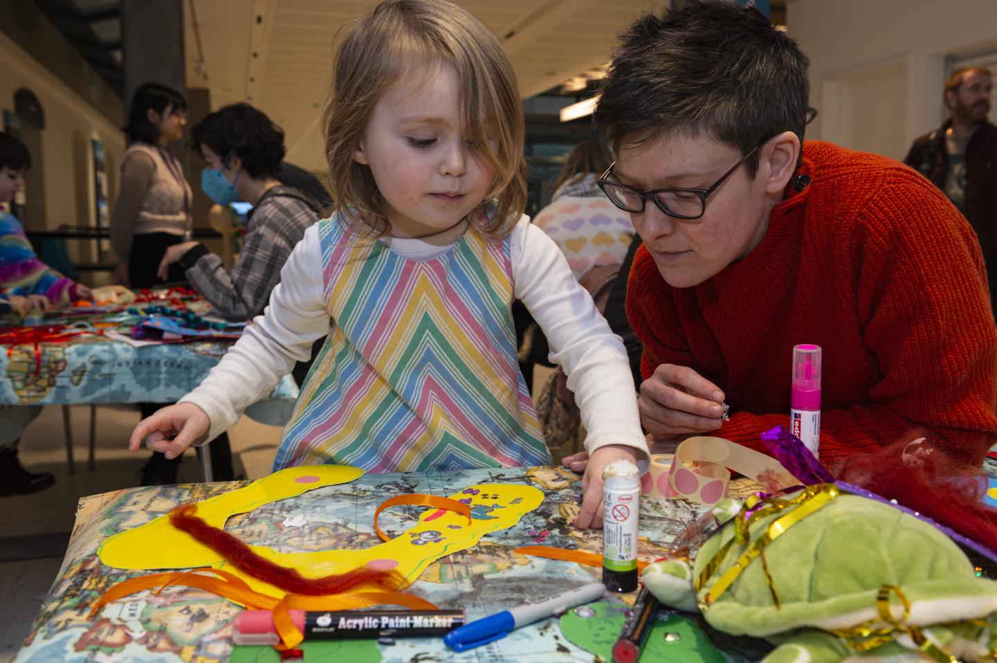 Child and adult standing next to table with lots of crafty materials on it