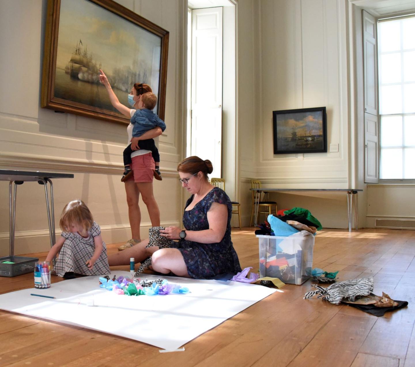 Families create portraits with craft materials on the floor of the Queen's House