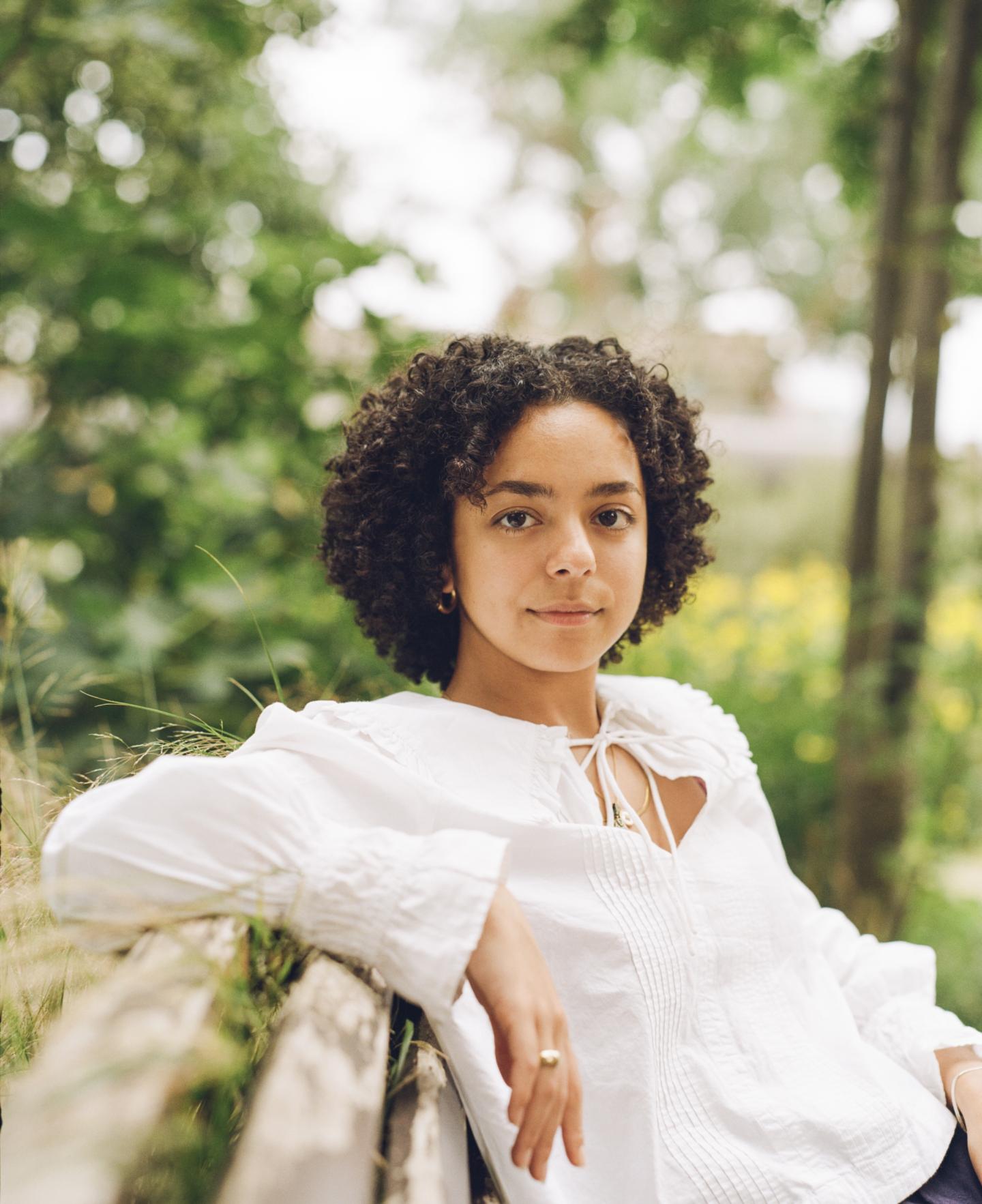 young woman leaning against a wooden structure with trees in background