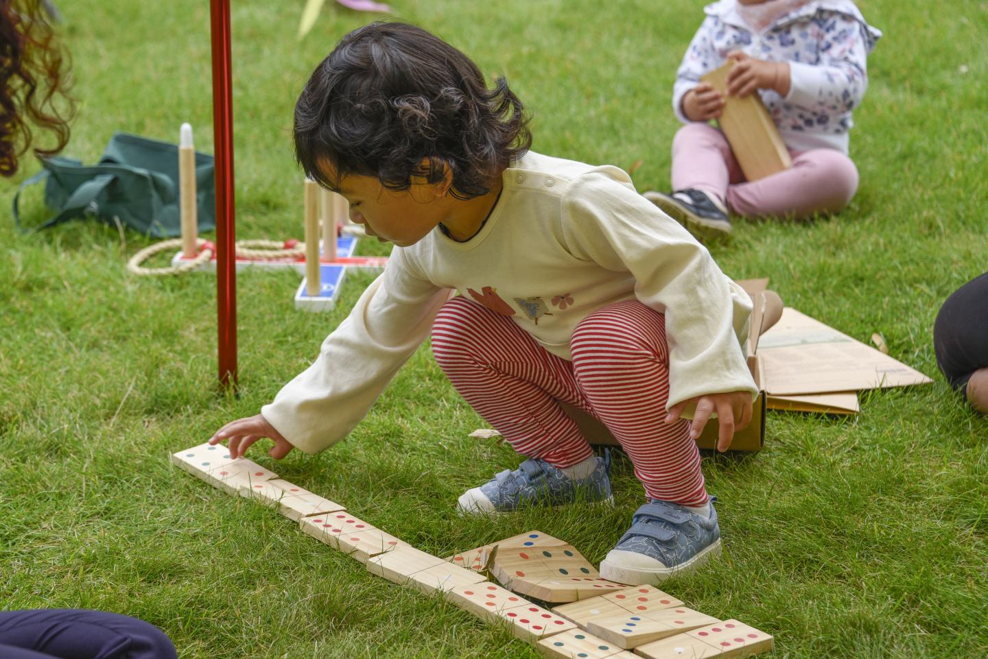 The image shows a young child playing with wooden dominoes.