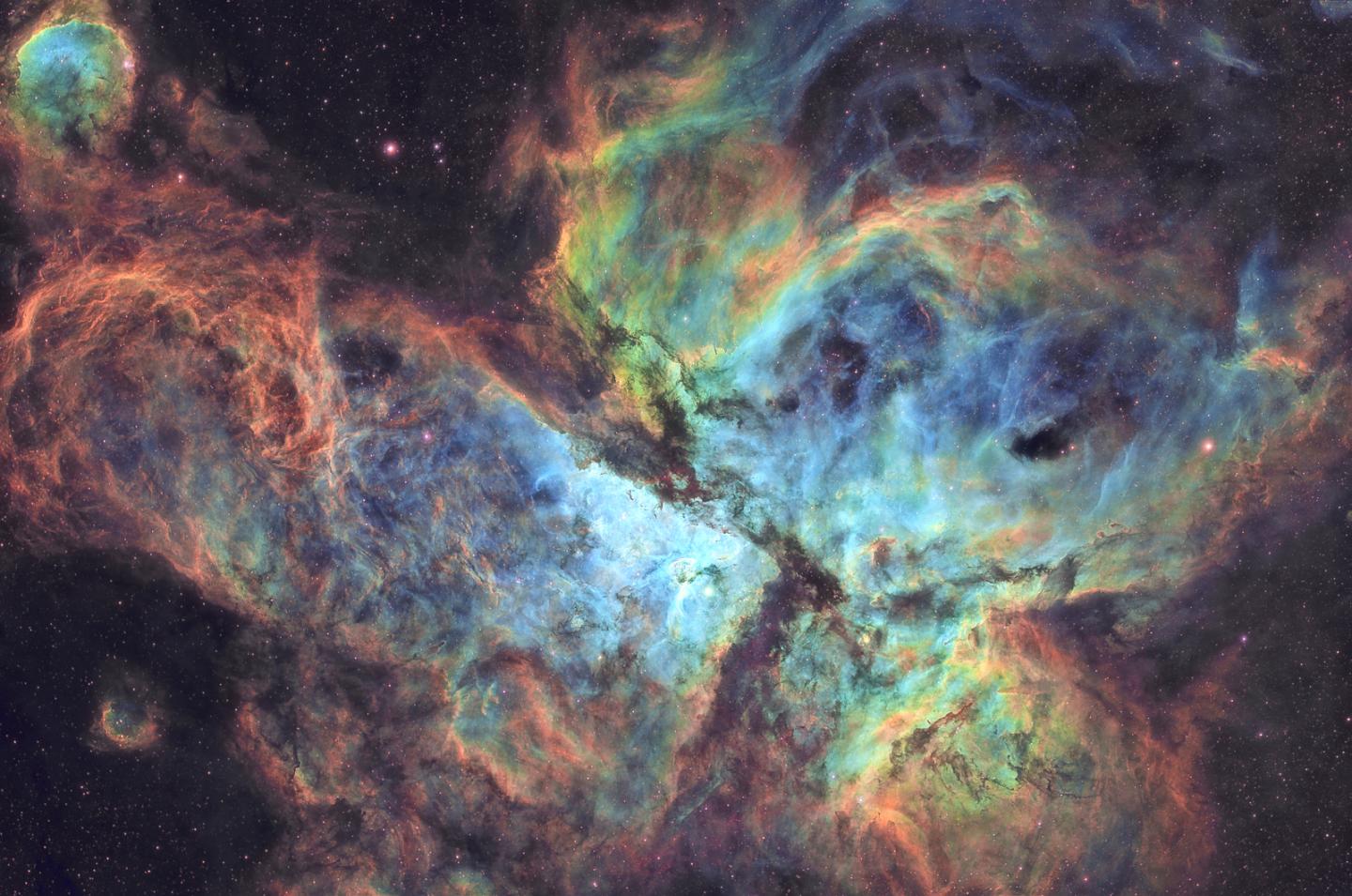 Deep space image showing the Carina Nebula, appearing as a swirl of pale blue and yellow mist against a dark sky