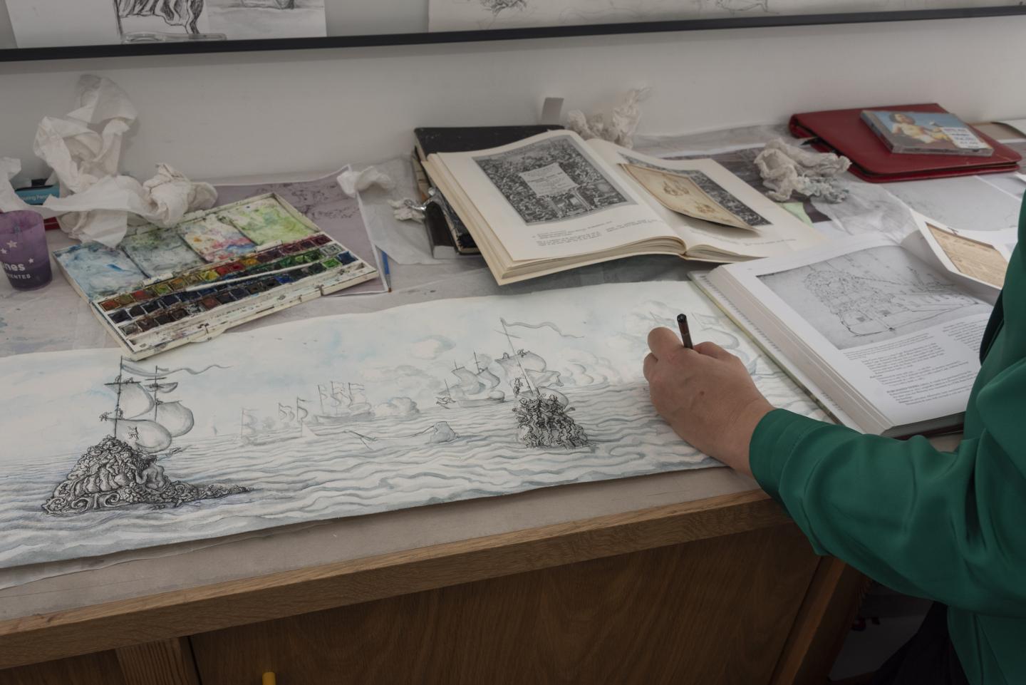 An artist sketches in a sketchbook surrounded by drawing materials