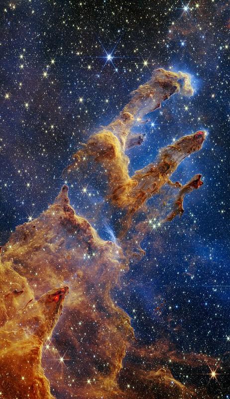 Image of nebula (gas and dust) in shape of 'pillars' which look like a human hand with fingers, in gold and yellow tones. The image is studded with hundreds of stars
