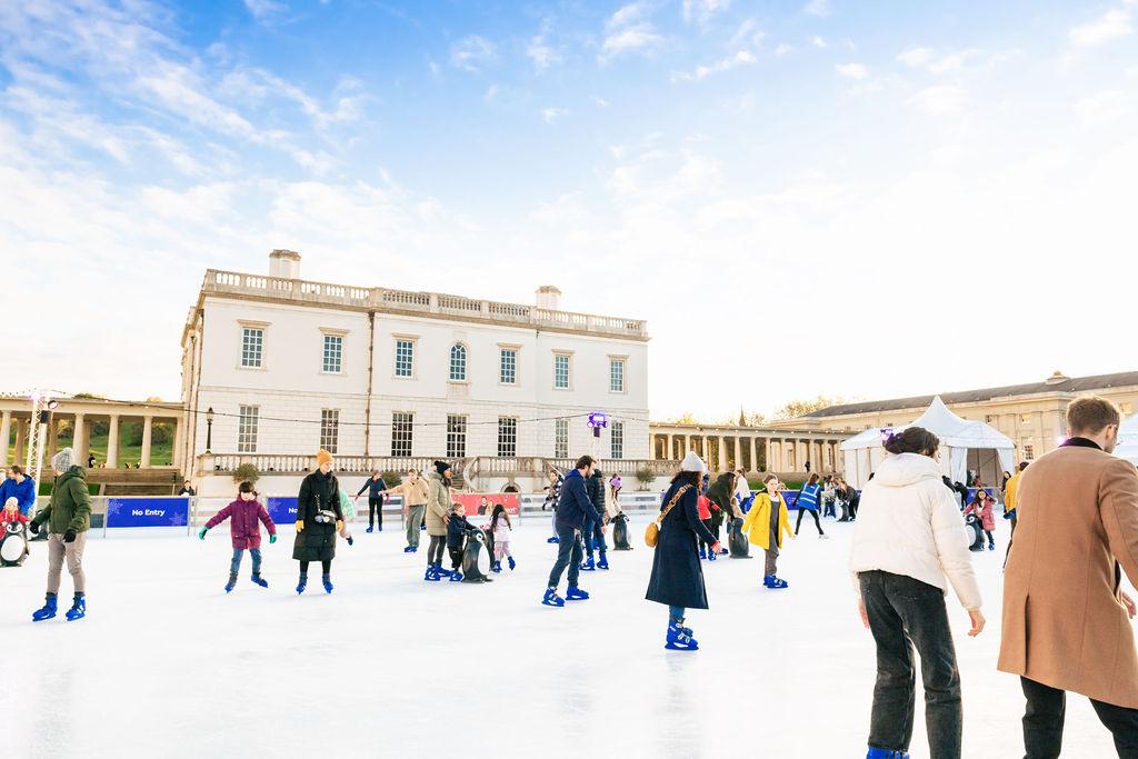 Image showing people skating on the Queen's House Ice Rink during the day, with a blue sky with thin clouds in the background