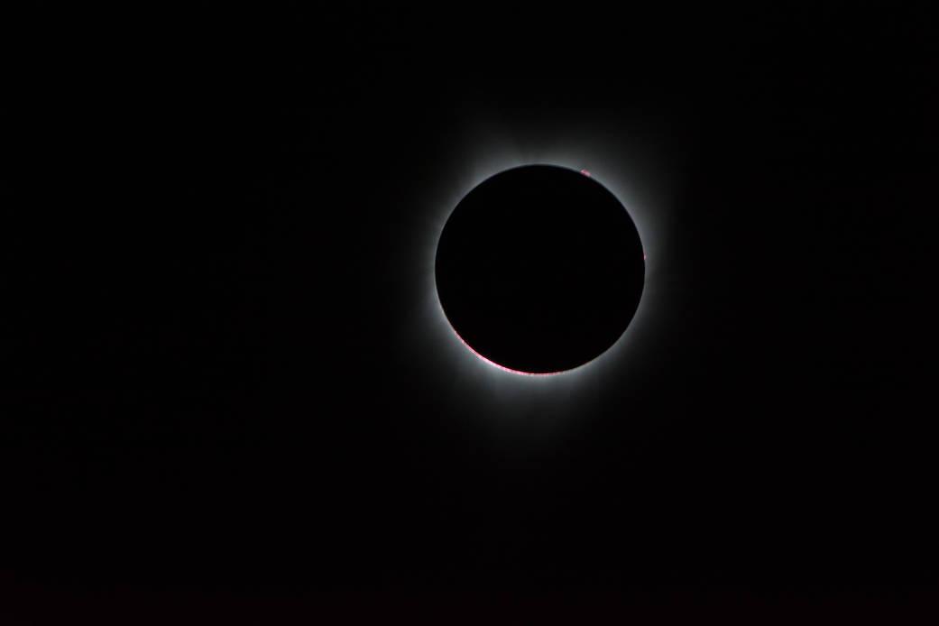 Image of the Sun with the Moon in front of it, with solar corona coming out from behind the circular Moon