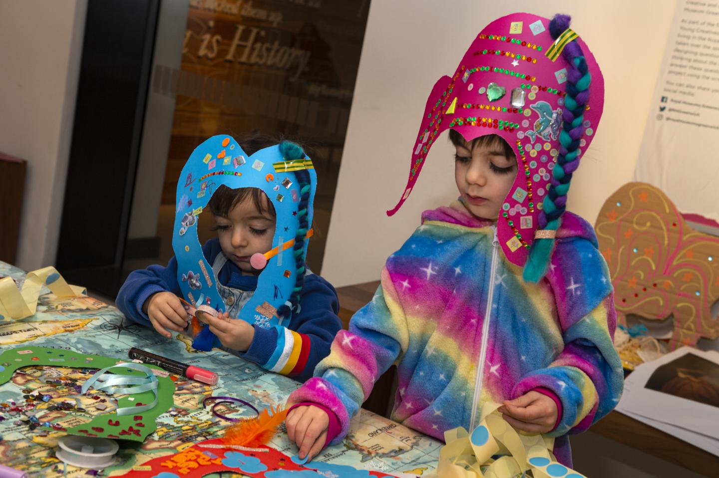 Two children making their own cardboard wigs