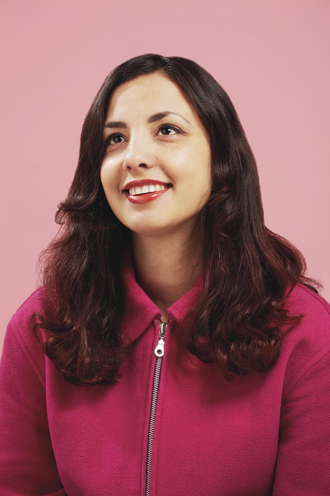 Colour photo headshot of a woman smiling against a pink background