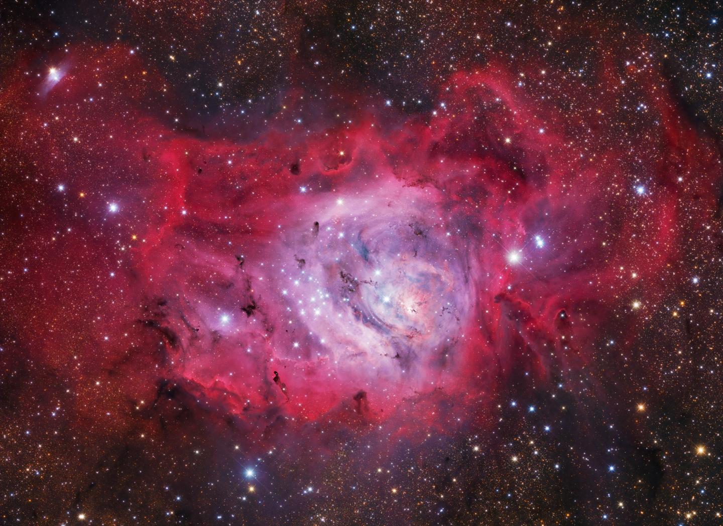 Image of the lagoon nebula, which has many bright blue stars in the centre within a rose pink cloud, surrounded by a darker pink cloud