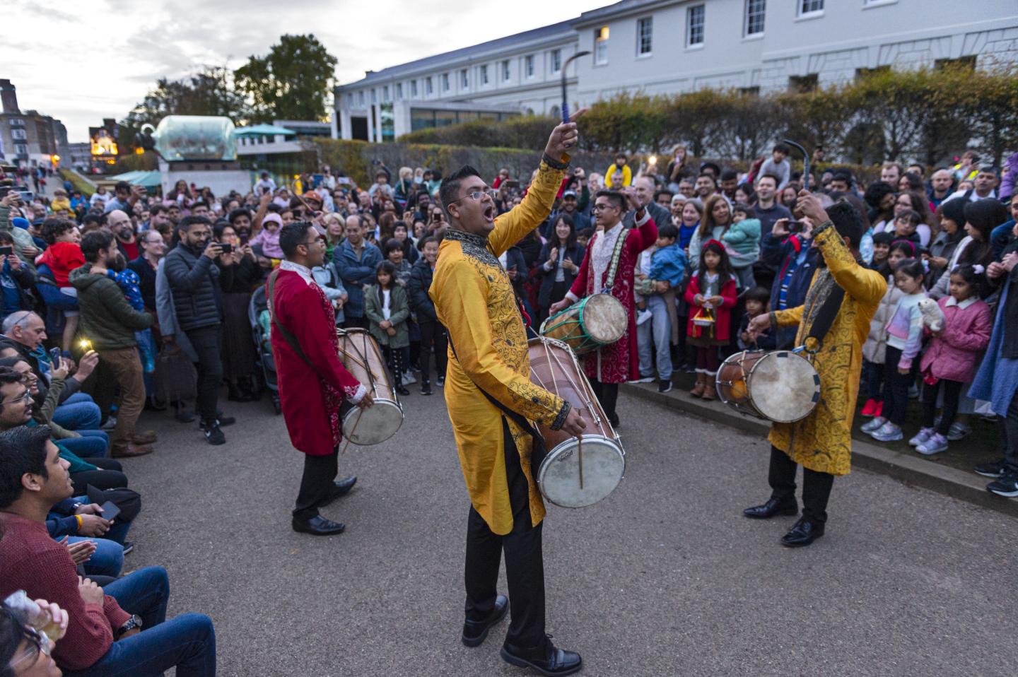 The image shows 4 men with drums surrounded by a crowd of onlookers.