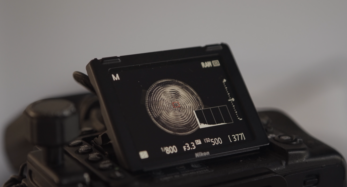 Image of a DSLR camera taking a photo of a petri dish of water with vibrations running through it