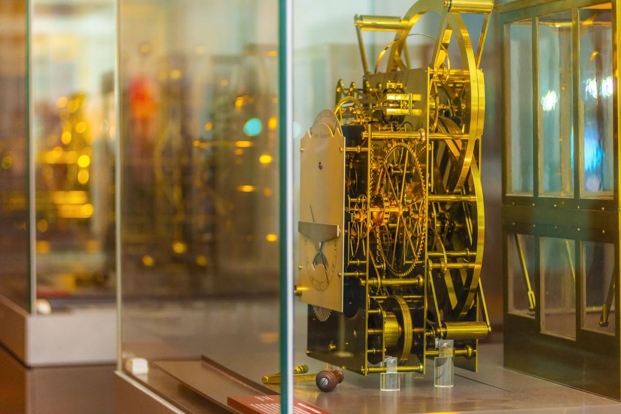 A sumptuous golden clock with its inner mechanism visible, on display in a glass case at the Royal Observatory Greenwich