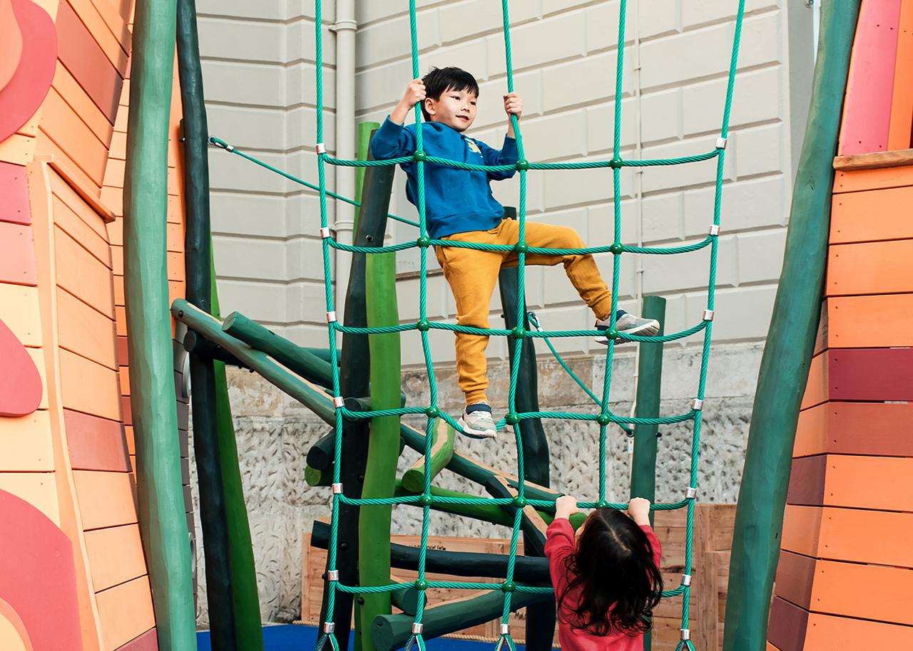 A boy climbs a cargo net in the National Maritime Museum's new playground, with his sister looking on from the ground