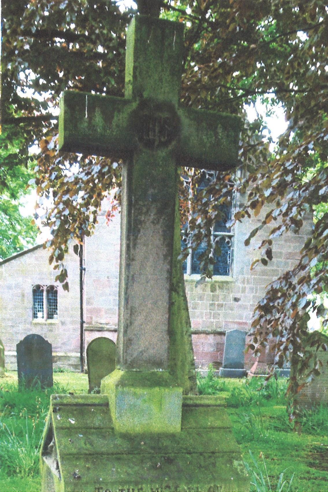 A grey sandstone headstone in the shape of a cross