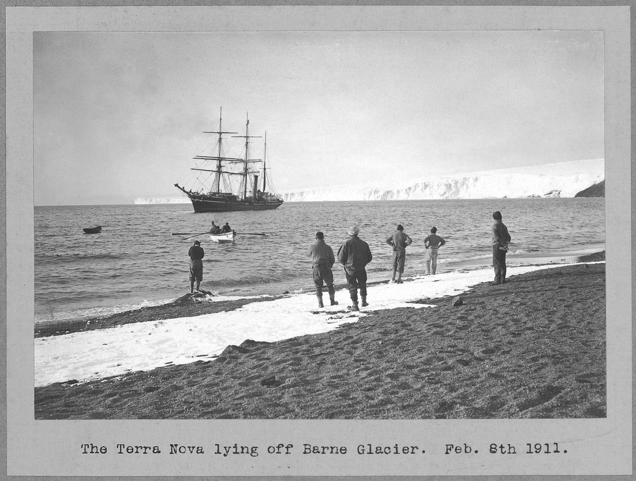 Image of the ship Terra Nova off the coat, with people standing on the shore looking out to sea