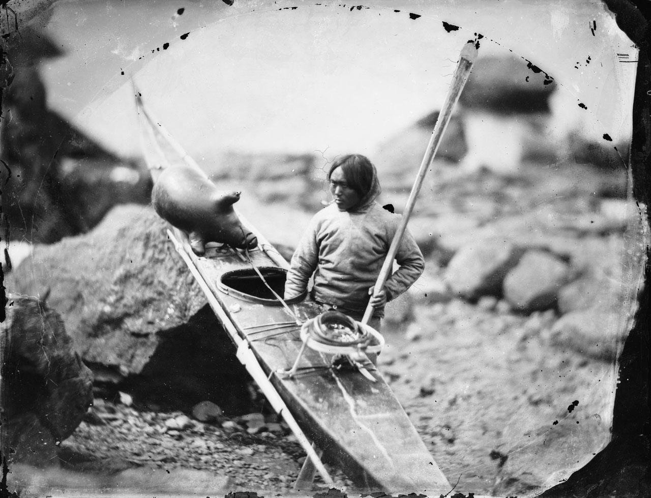 Historic black and white photograph of an Inuit man holding a kayak