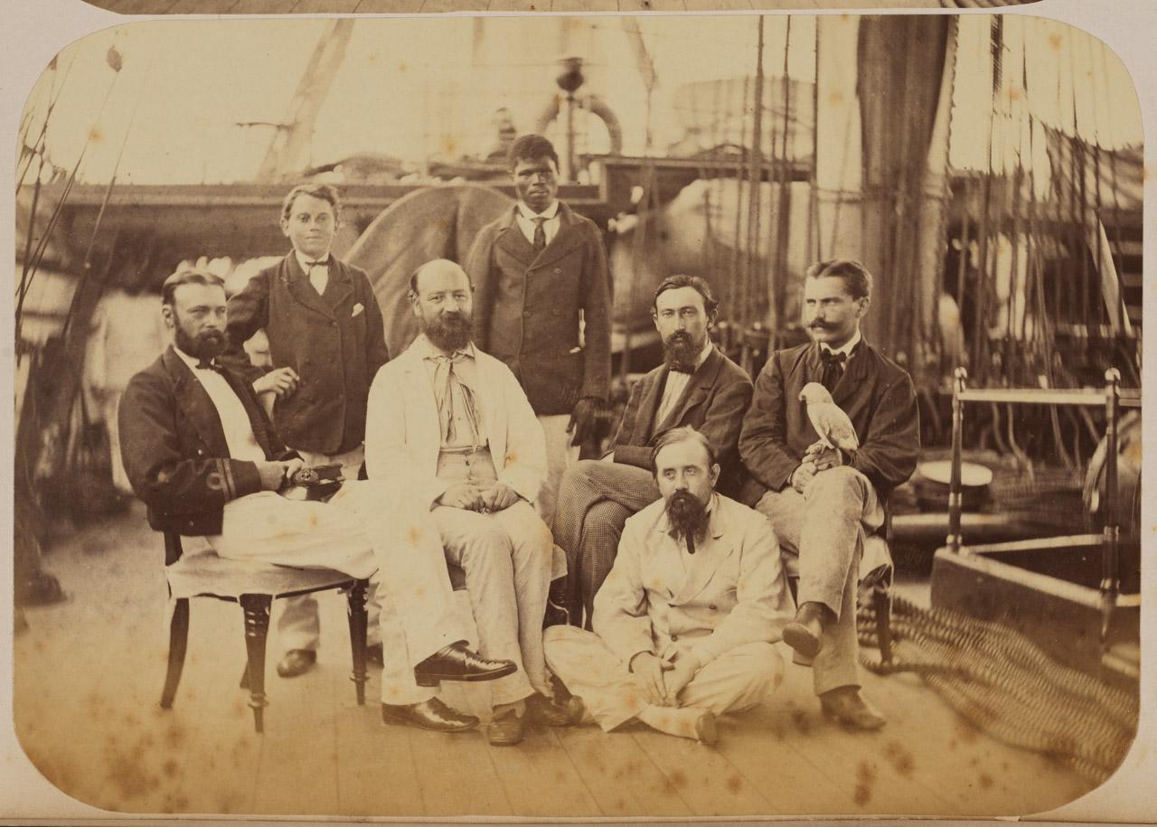 Sepia-tone photograph taken on board HMS Challenger showing the naturalists and two of their assistants, part of an album of photographs from the Challenger expedition of 1875