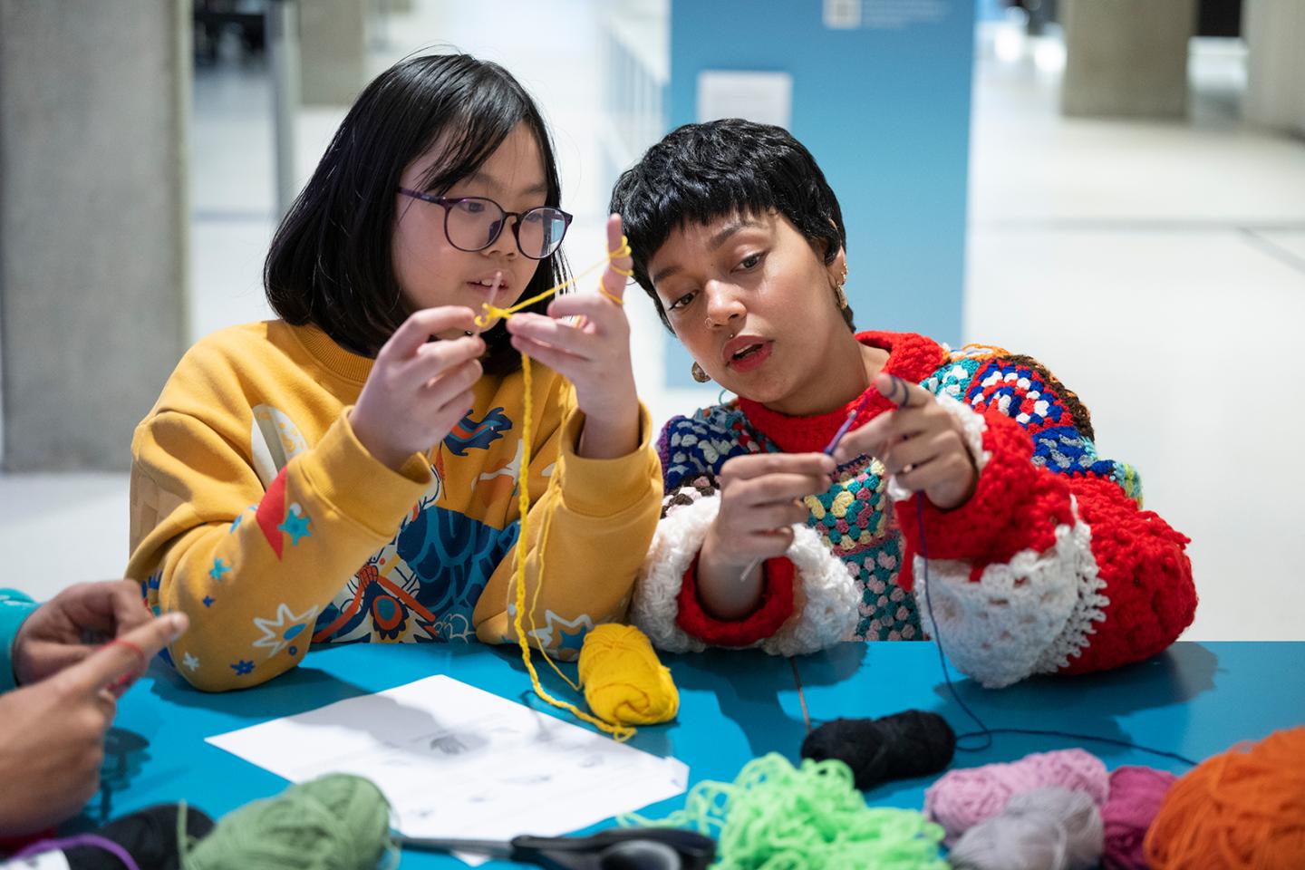 Two people work on a craft activity using woolen thread