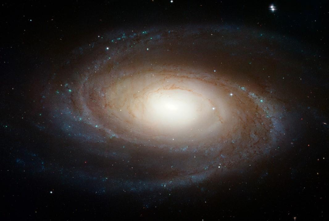 A photograph of a galaxy with blue spiral arms of stars and a yellow glowing centre. 