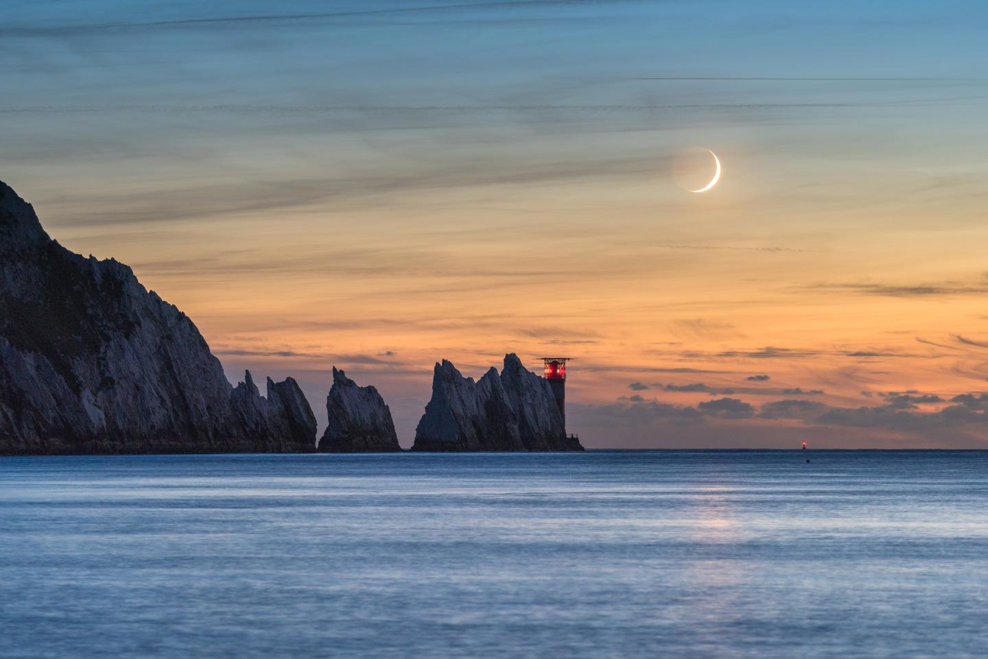 Crescent Moon at sunset with mountains in the background and sea in the foreground