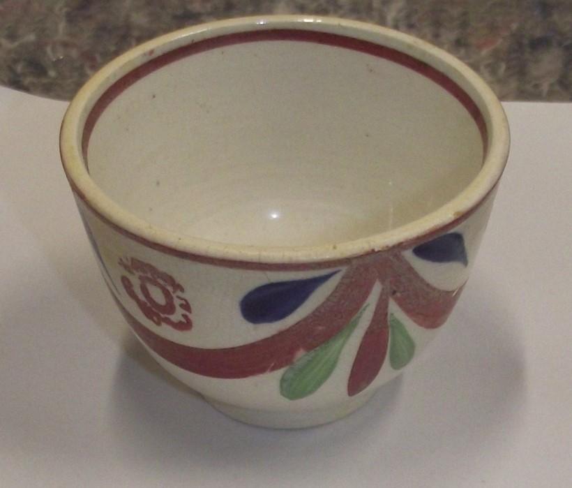white ceramic teacup with a blue, red and green design on the front 