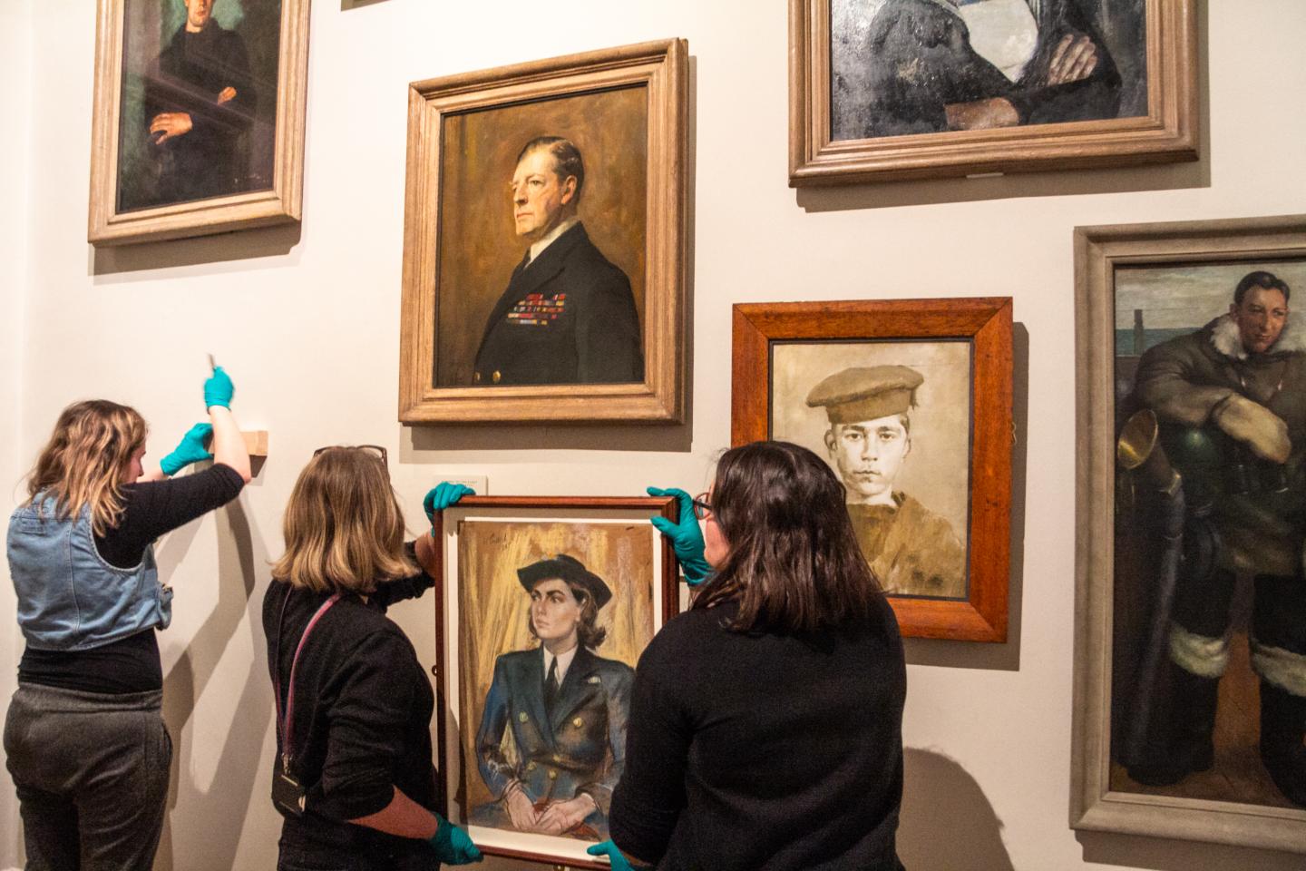 Art handlers prepare to lift a portrait of a Wren officer into place