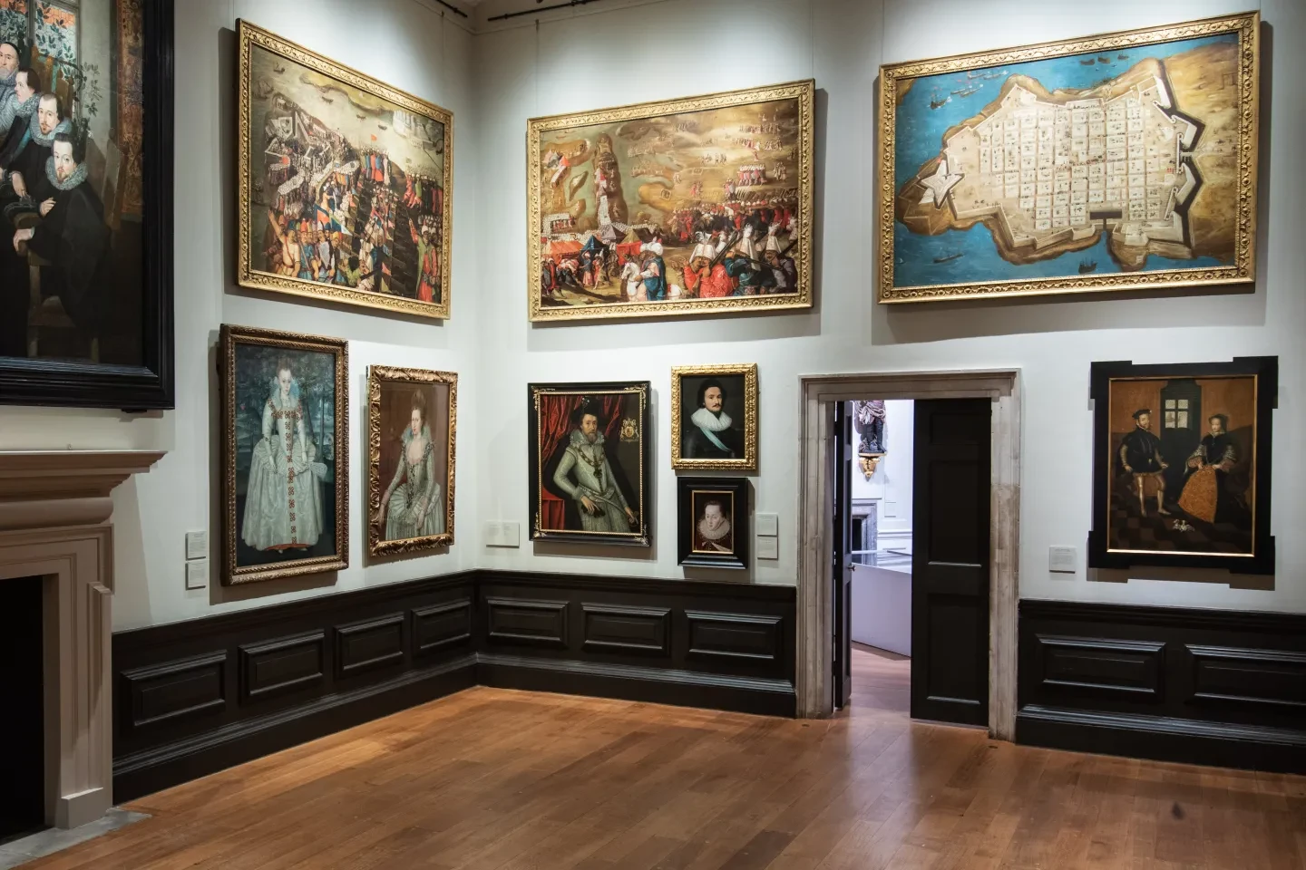 A gallery wall of large paintings on display in the Queen's House, with an open doorway in the middle