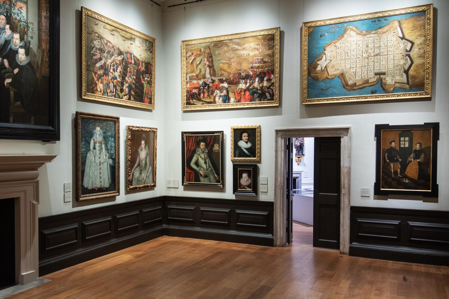 A gallery wall of large paintings on display in the Queen's House, with an open doorway in the middle