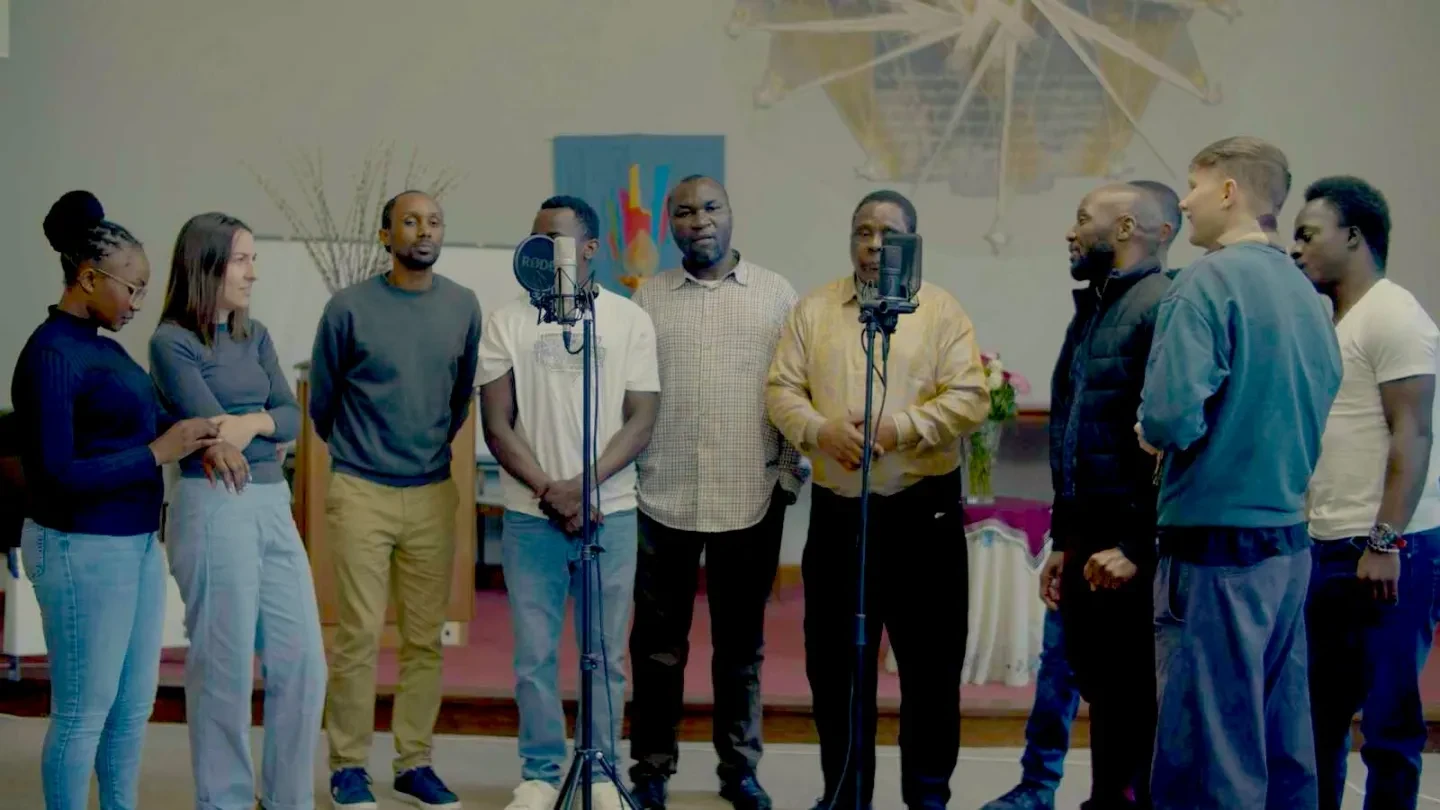 Photo of a group of people, standing and singing to microphones