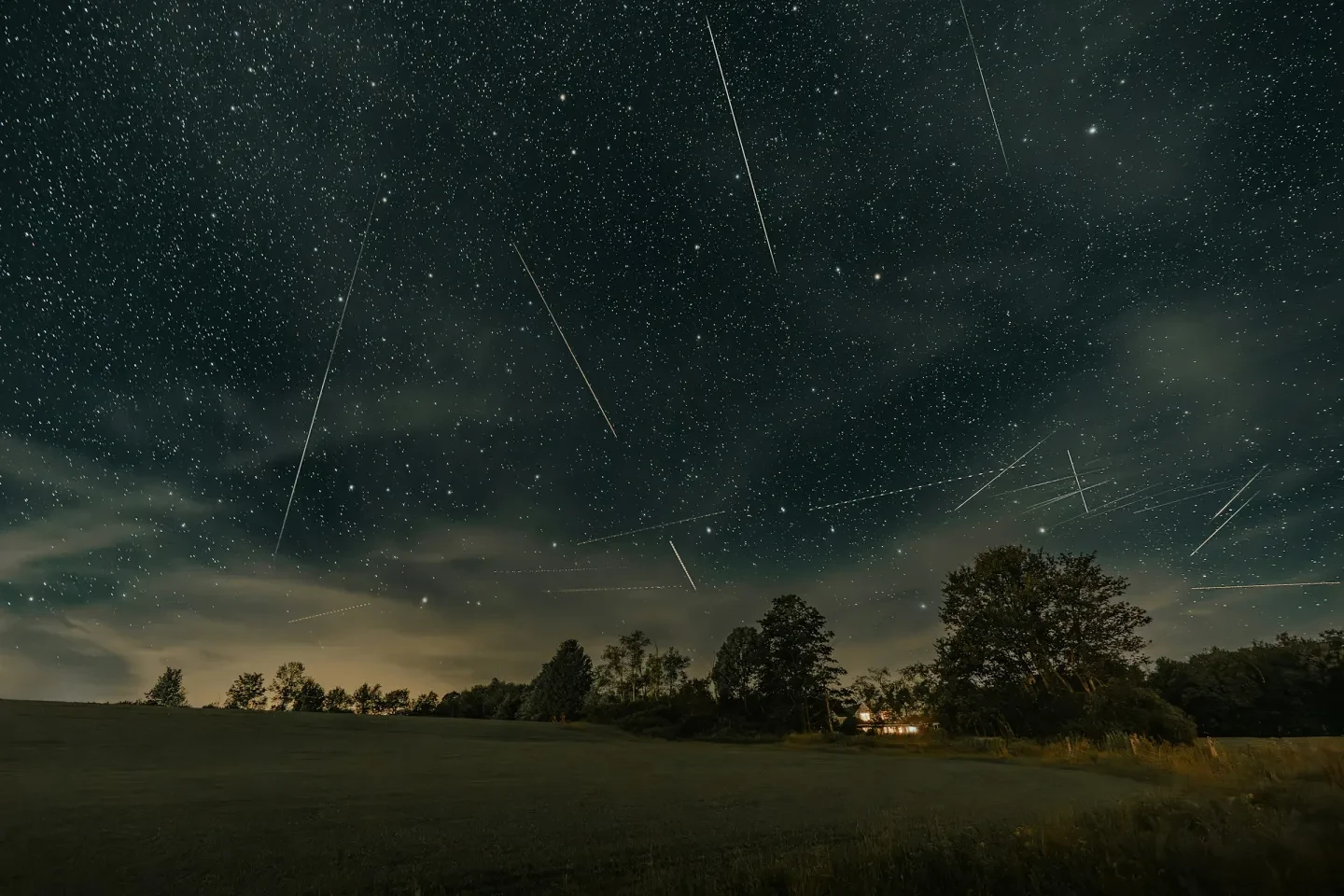 Photo of a landscape at night with streaks in the sky which are Perseid meteors raining down