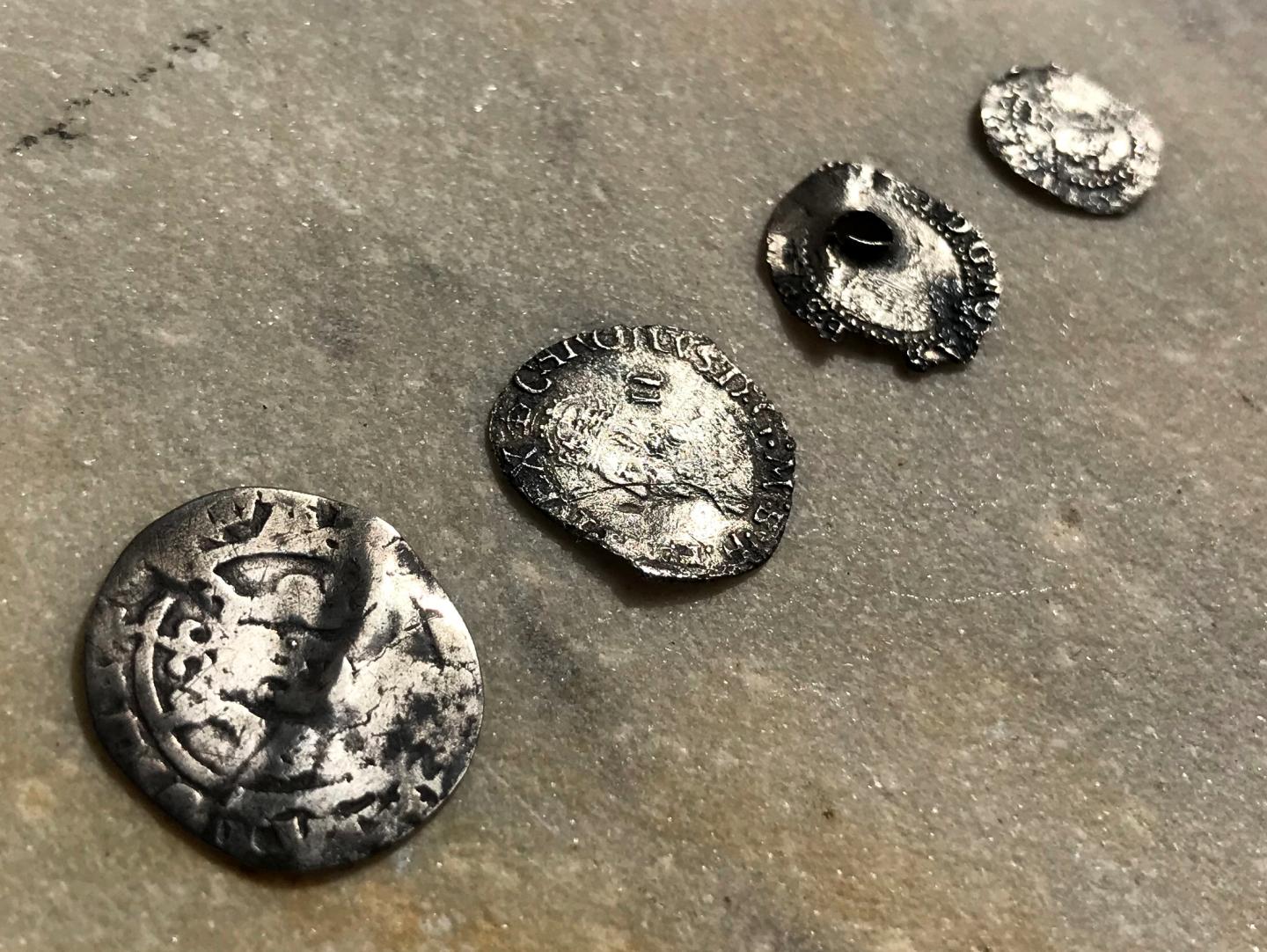 A row of four old silver coins laid out on a paving stone