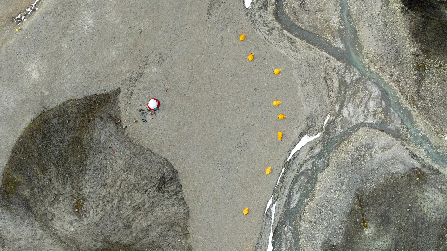 Drone photo showing the base camp in Purple Valley, Ellesmere Island. A white and red mess ten is on the left, and a series of yellow tents visible in a line on the right