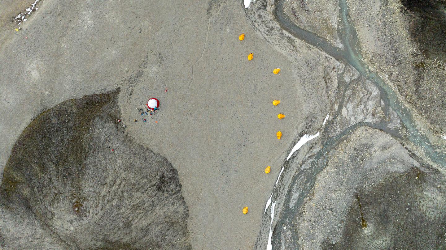 Drone photo showing the base camp in Purple Valley, Ellesmere Island. A white and red mess ten is on the left, and a series of yellow tents visible in a line on the right
