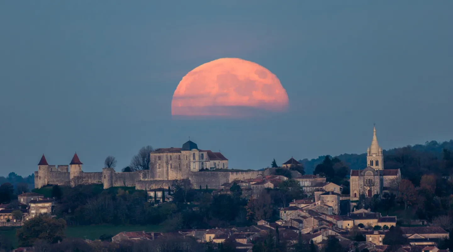 Landscape photo of French town called Villebois-Lavalette with a large orange moon in the sky with the top half visible