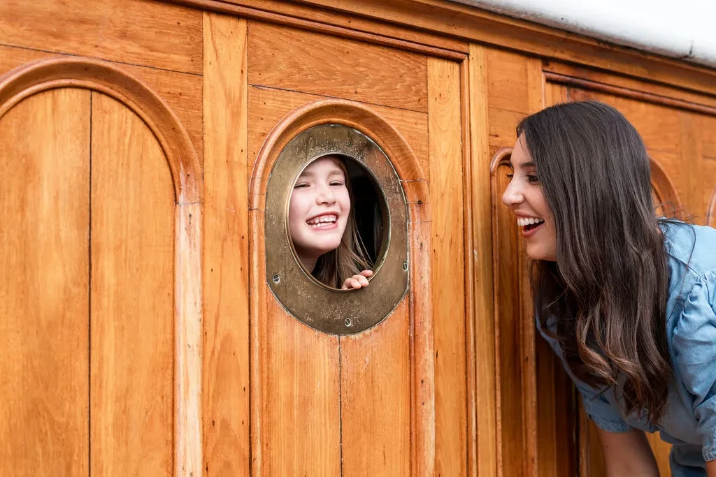 Mother and daughter looking through porthole on Cutty Sark from opposite sides and smiling