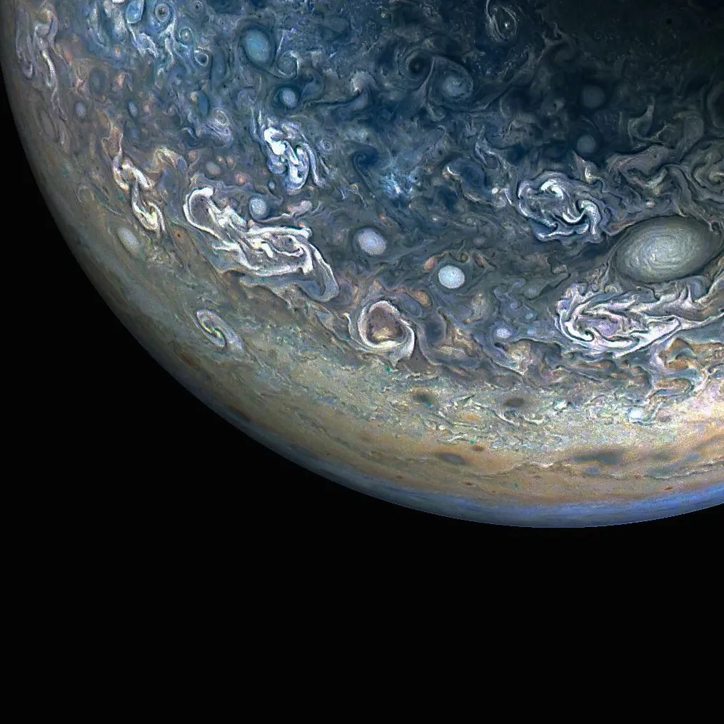 Colour-enhanced view of Jupiter captured by the Juno NASA mission. Swirling clouds of white, blue and gray fill the upper right corner of the image where the planet's surface can be seen