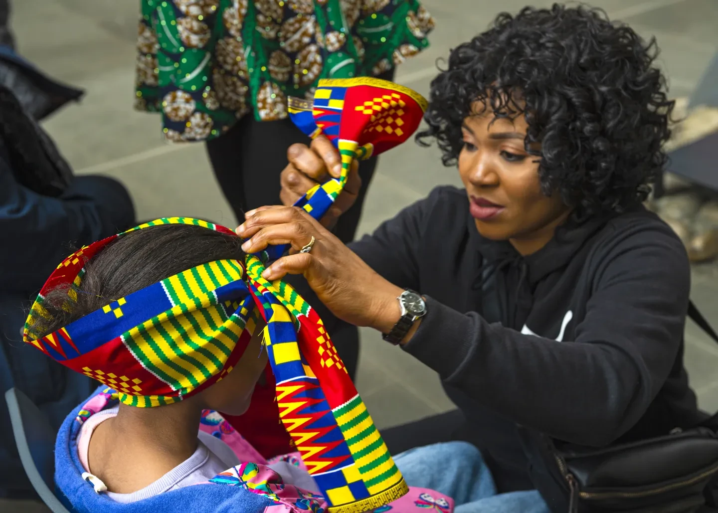 A woman wraps a colourful headdress around the head of a young girl