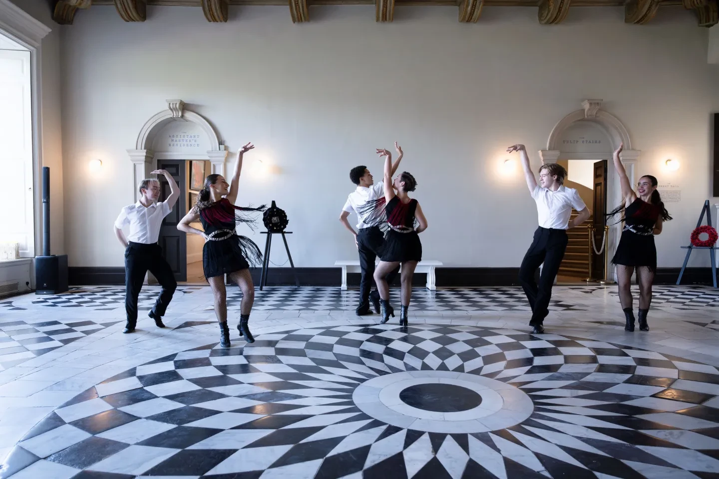 A group of dancers perform on a black and white marble floor in the historic Queen's House