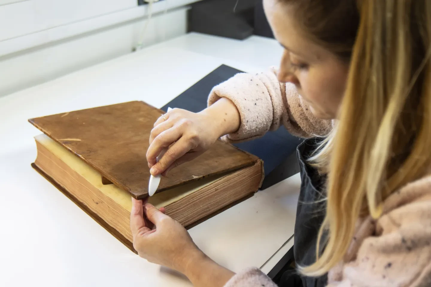 A woman doing conservation work on a large old-looking leather-bound book
