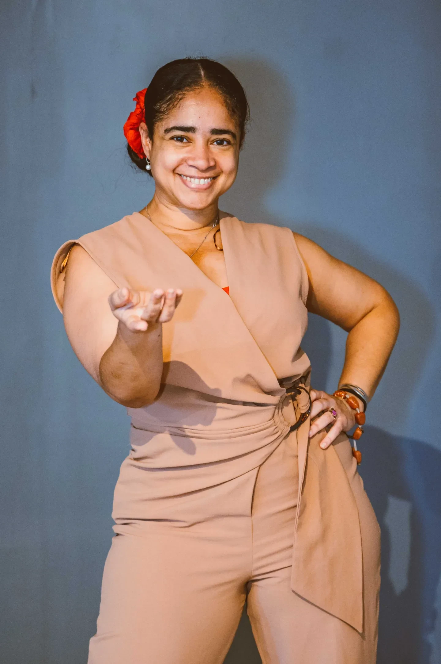 A smiling woman with flowers in her hair stands with her hand on her hip, reaching out towards the viewer with her other hand, an invitation to dance