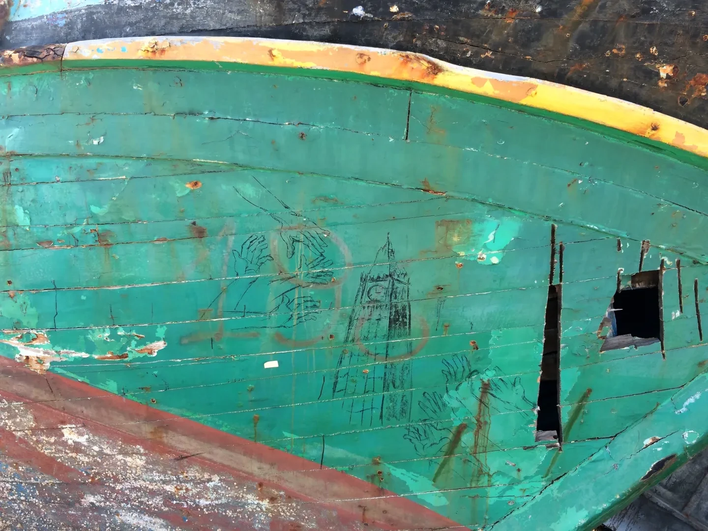 A photograph of a drawing found on the side of a small boat. The boat is green with a yellow band, and the drawing shows hands reaching out to a depiction of the Elizabeth Clock Tower in London