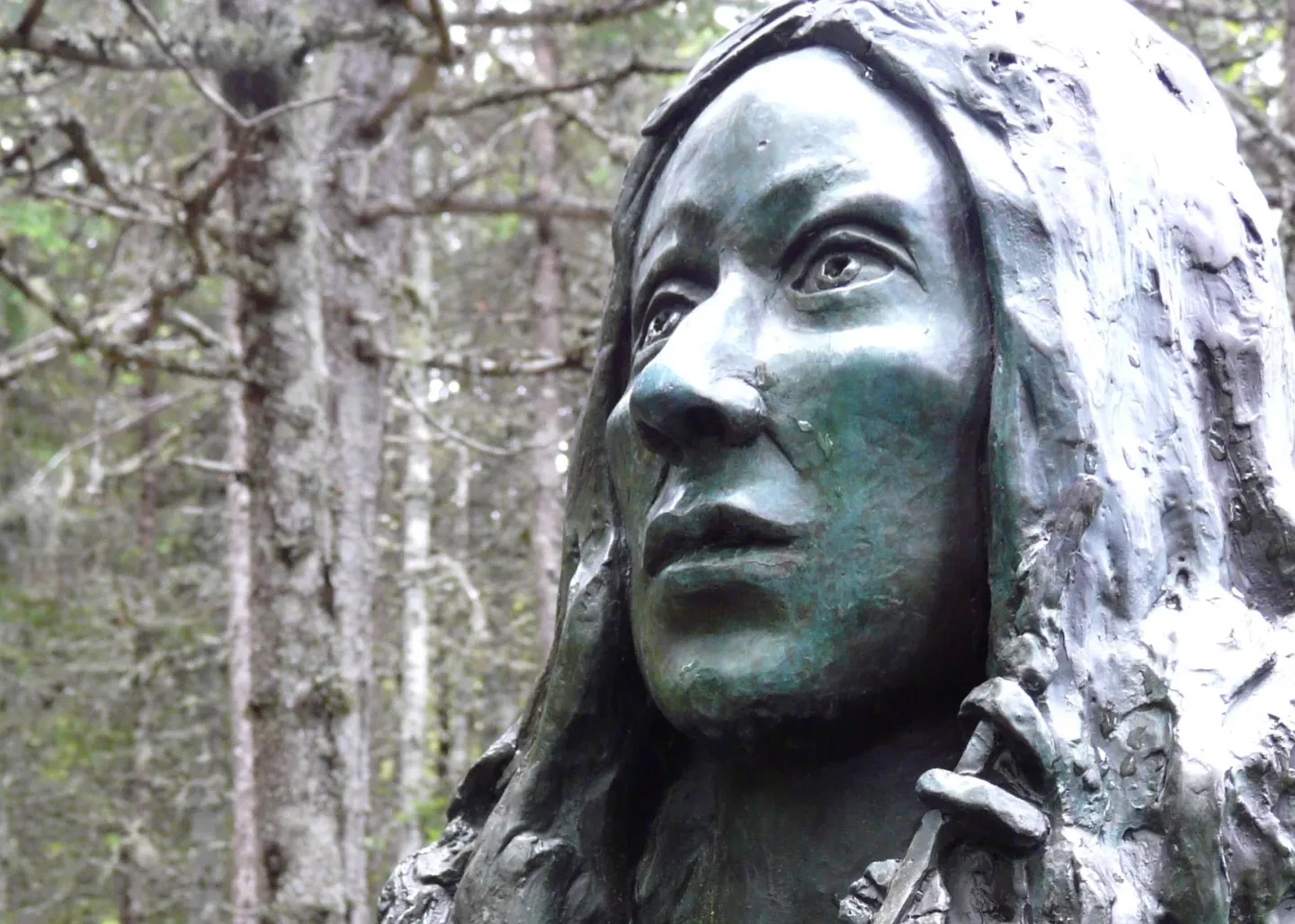 A bronze statue of a woman situated among the trees