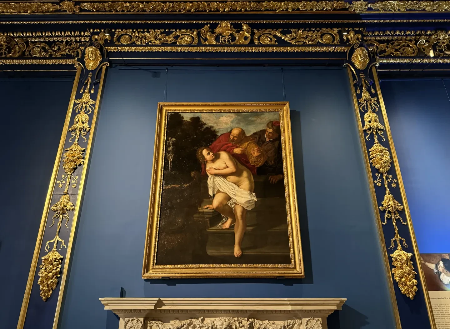 Painting of Susanna and the Elders on display in a blue and gold room