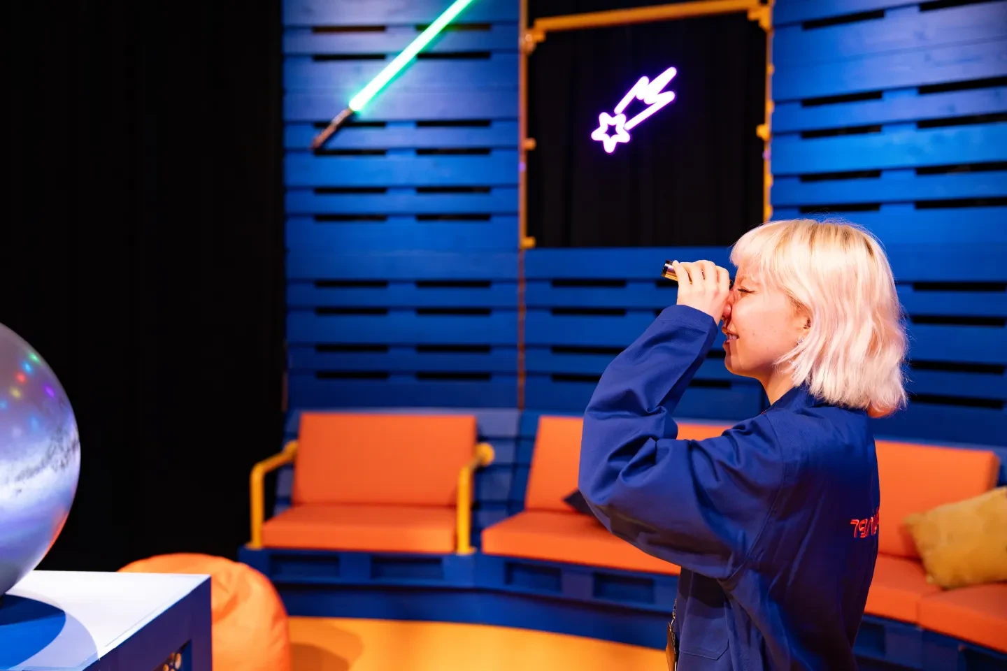 An astronomer in a blue boilersuit looks through a starlight splitter in a blue room with orange sofas